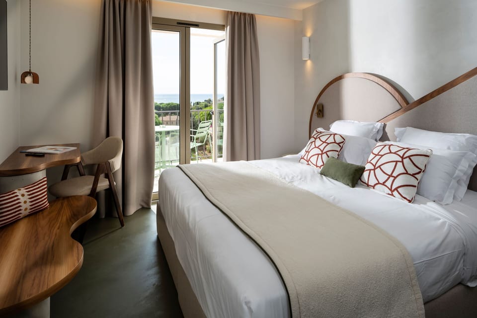 Large bed with decorative pillows and a writing desk, with glass doors opening to the sea-view balcony