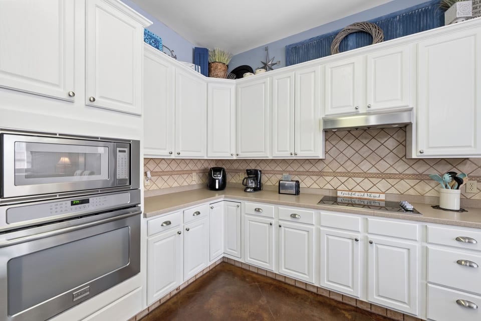 Your fully equipped kitchen features white cabinetry, stainless appliances, and a charming tile backsplash—perfect for preparing meals and gathering over morning coffee.