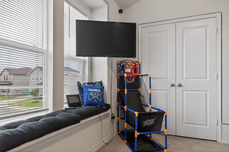 A cushioned window seat, wall-mounted TV, and an indoor arcade basketball hoop.