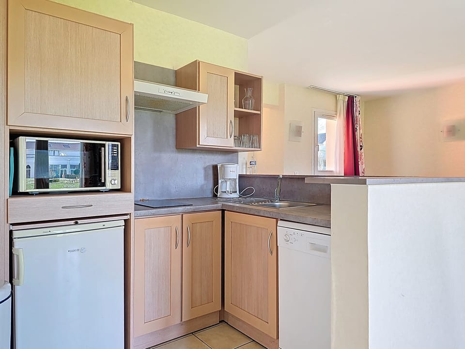 Kitchen with light wood cabinets, white microwave and dishwasher, grey countertop, and space for a full group