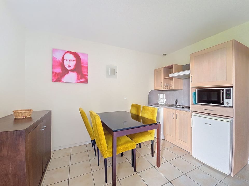 Kitchenette with light wood cabinetry, yellow dining chairs, and a pink artwork print on the wall