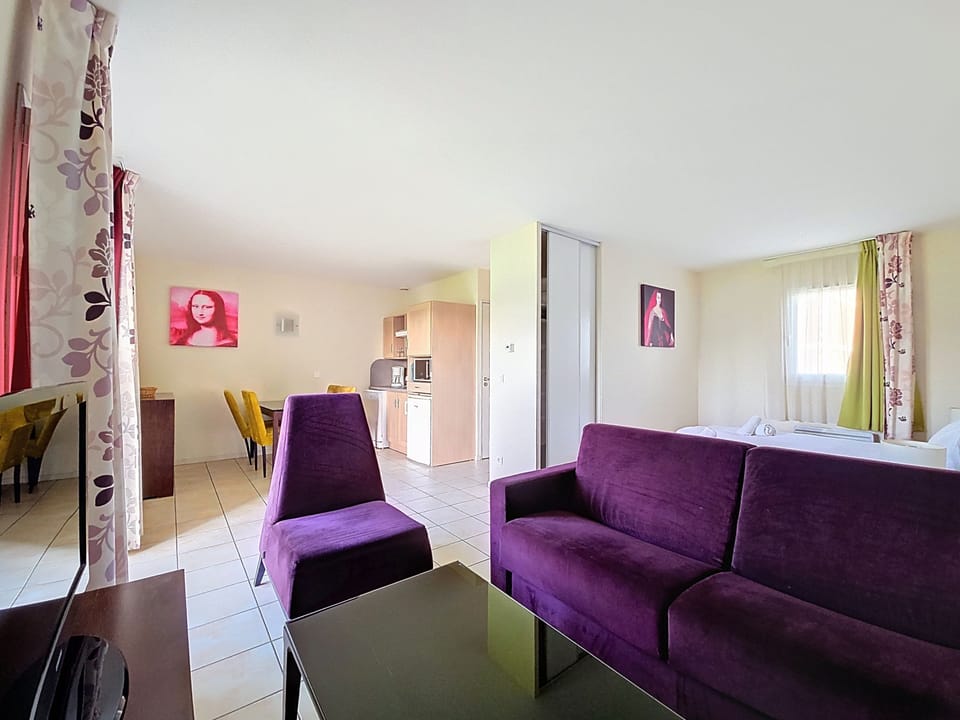 Open-plan layout combines dining area and kitchenette — purple sofa and colourful artwork visible throughout