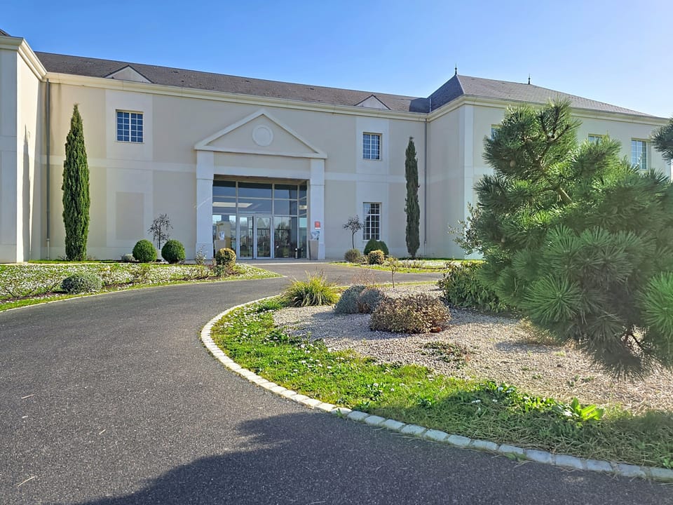 Tree-lined pathway leading toward the main entrance, flanked by low shrubbery on both sides