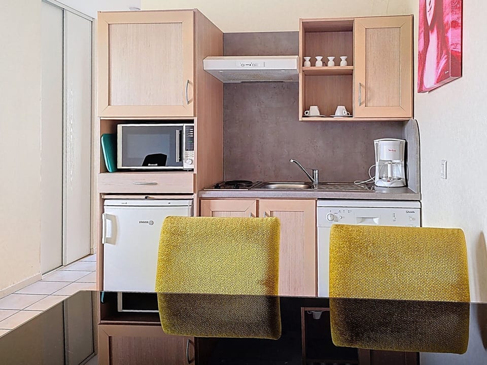 Kitchen corner with light wood cabinets, microwave, dishwasher, and fridge — green dinnerware on the shelf