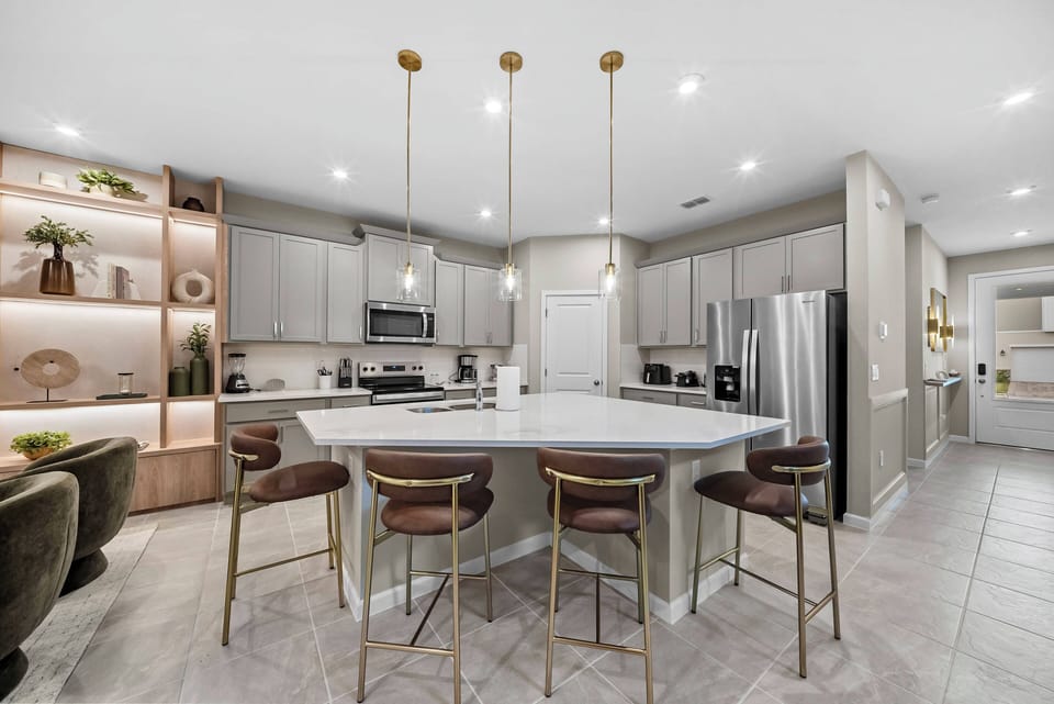 Experience the charm of this stylish kitchen, featuring a spacious island, sleek white countertops, and modern pendant lights. With warm wood accents and soft gray cabinetry, it's a cozy and sophisticated space ideal for.
