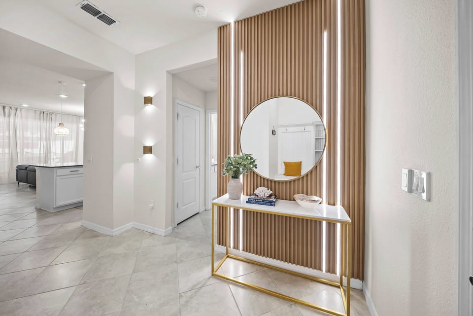 Enter a beautifully designed space with warm wood paneling and a sleek round mirror that enhances the light and style. A chic gold-accented console table adds decorative touches, creating an inviting welcome for your stay.