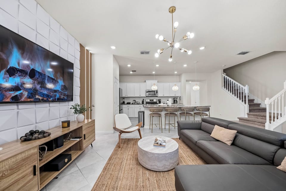 Relax in this spacious living area with a sleek black leather sectional and a stylish round coffee table. A modern chandelier casts a warm glow over the textured rug, making it perfect for cozy movie nights with a large TV.