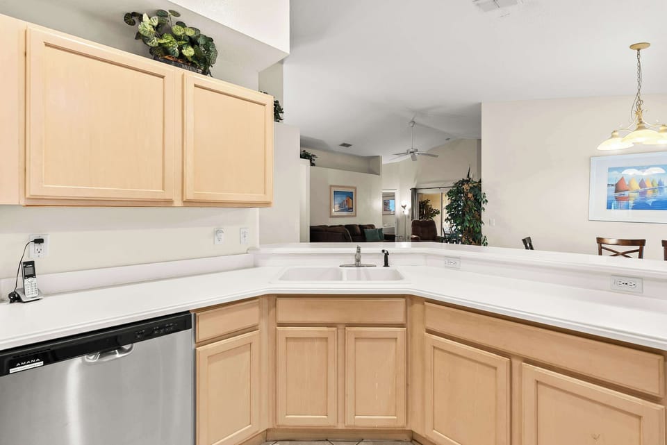 Modern kitchen with light wood cabinets and stainless steel dishwasher overlooking the living area