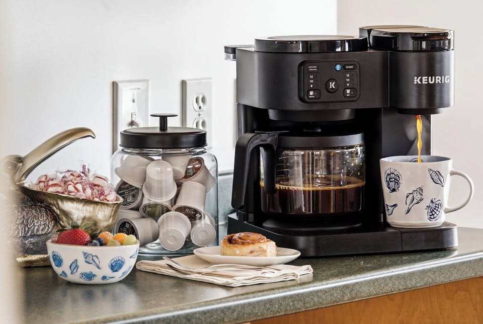 Fully stocked coffee station featuring a Keurig, drip coffee maker, mugs, and complimentary coffee essentials.