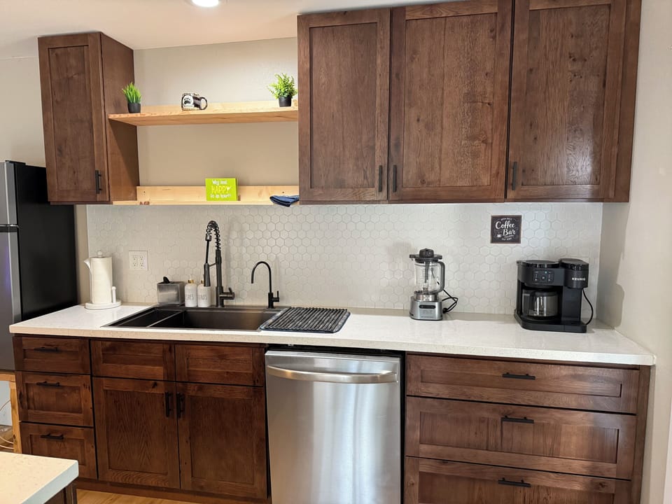 Modern kitchenette with coffee station, dishwasher, and warm wood finishes