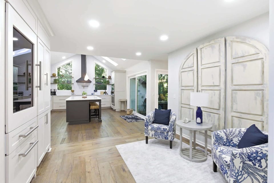 White custom cabinetry, a charcoal center island, and blue-and-white coral print accent chairs beside a dramatic distressed arch installation make this kitchen-nook one of a kind.