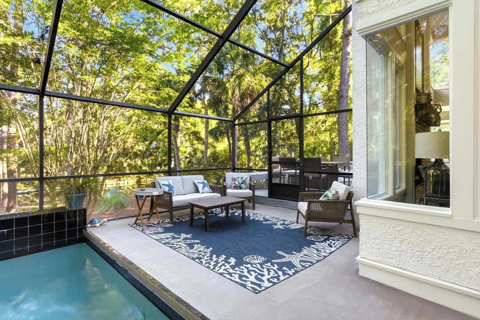 The screened patio features lounge seating, a coffee table, and a coral rug right beside the pool — a shaded, bug-free space to relax all day long.