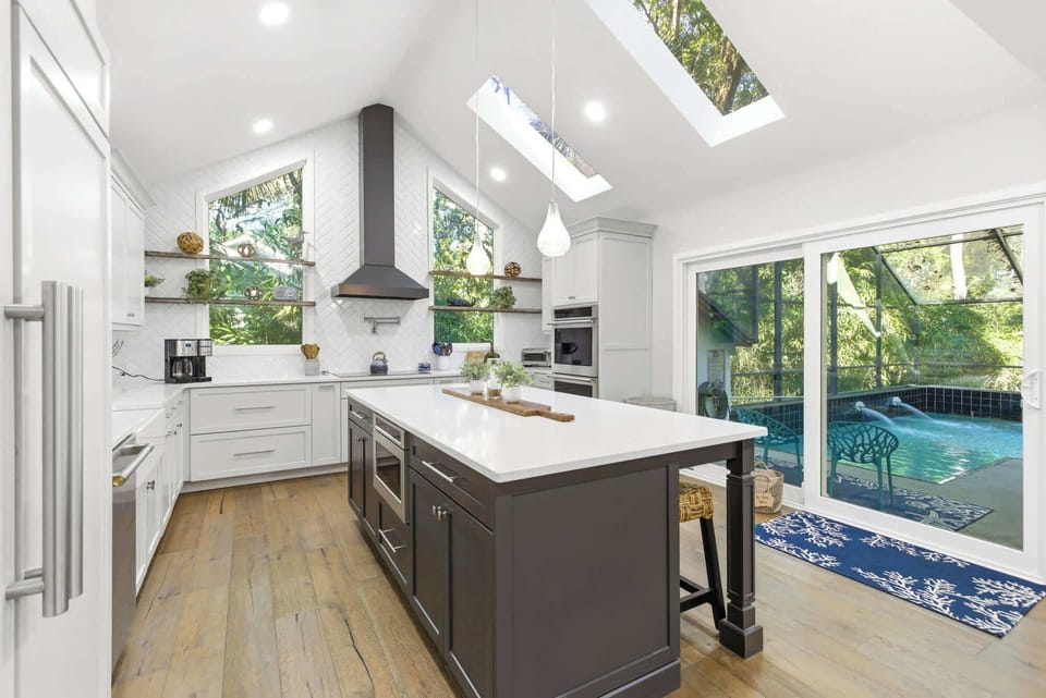The kitchen's large island, herringbone backsplash, double wall ovens, and built-in appliances are all framed by a pool-side slider that keeps the outdoors close.