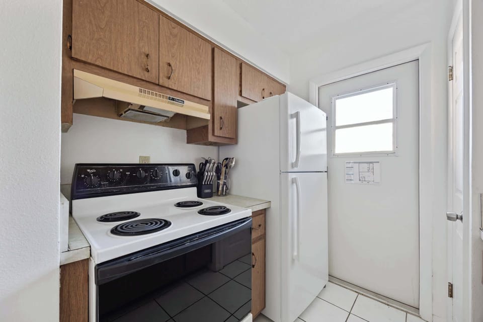 Compact kitchen with electric stove, wooden cabinets, and a white refrigerator.