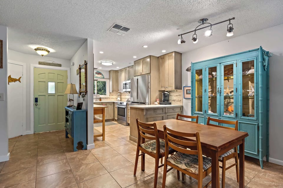 Dining area with a wooden table and a turquoise display cabinet next to a modern kitchen.