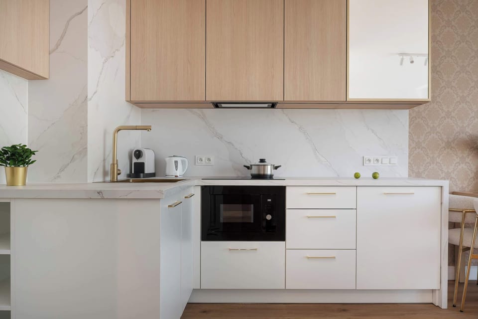 
A contemporary kitchenette with built-in appliances, white furniture, and wooden accents. The room feels bright and functional.