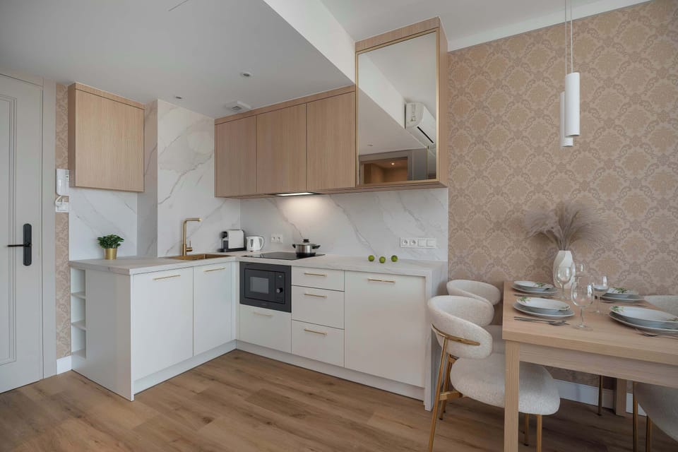 A bright kitchenette with white cabinets, wooden details, and modern appliances. The open layout gives the space a clean and spacious feel.
