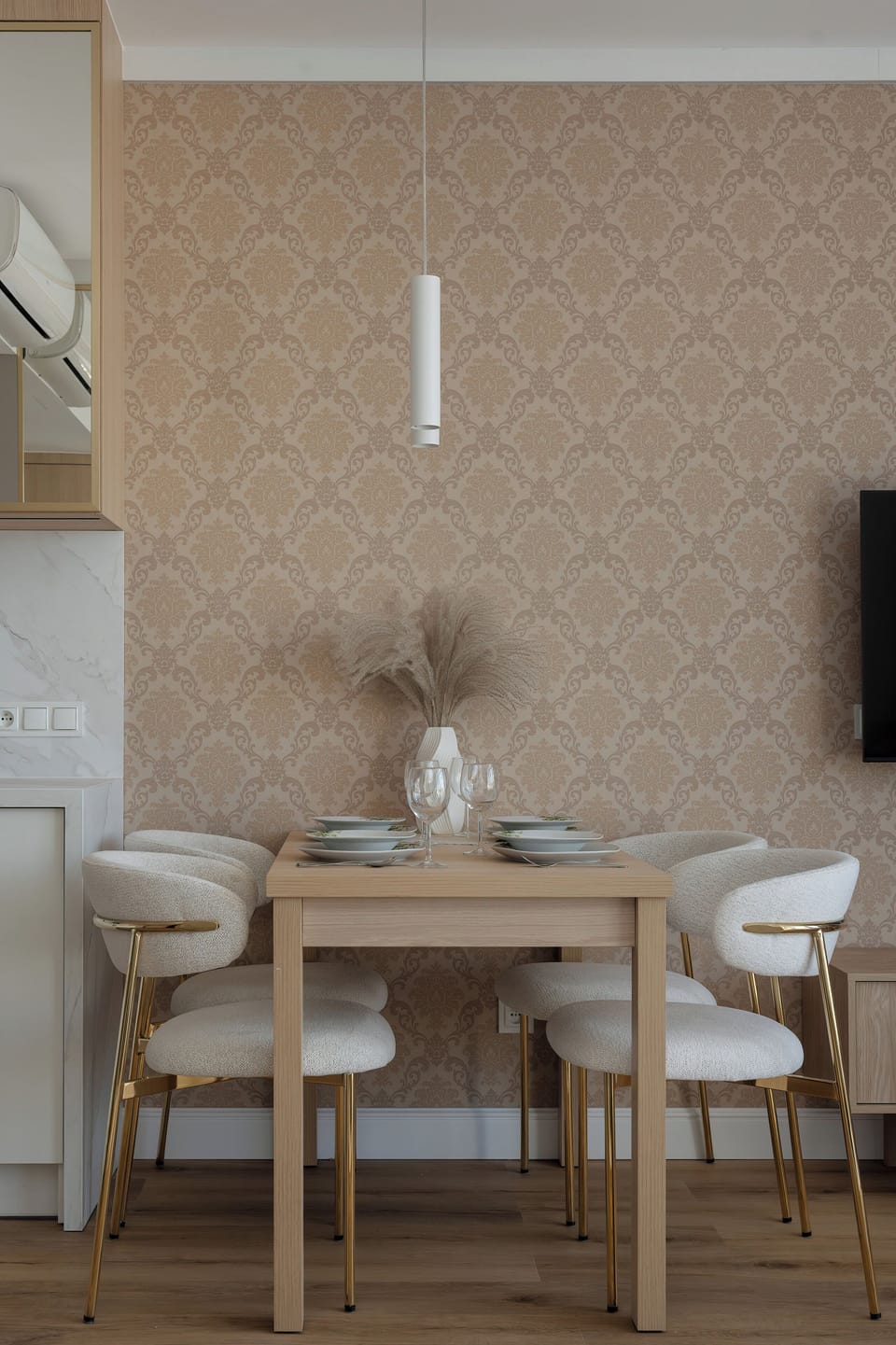 A modern dining area with a small table, elegant chairs, and warm beige decor. Soft lighting creates a cozy atmosphere.