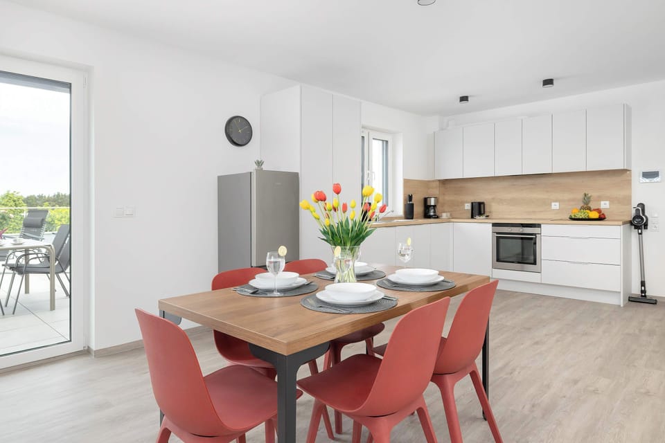 The dining room features a solid wooden table surrounded by red chairs and centered with a bouquet of colorful tulips. The space seamlessly connects to the white cabinetry of the kitchen.