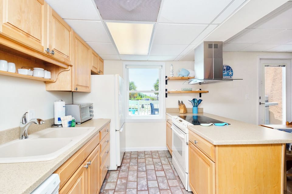 Your bright, fully equipped kitchen awaits, complete with modern appliances and plenty of counter space for preparing meals. Natural light pours in through the window, while sleek touches like open shelving add charm.