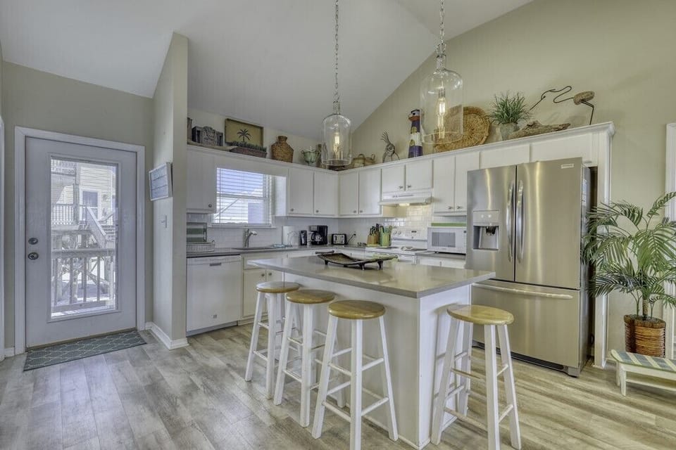 Picture yourself preparing meals in this bright, airy kitchen with gleaming stainless appliances, coastal-chic lighting, and a handy island with seating—perfect for morning coffee or evening gatherings.