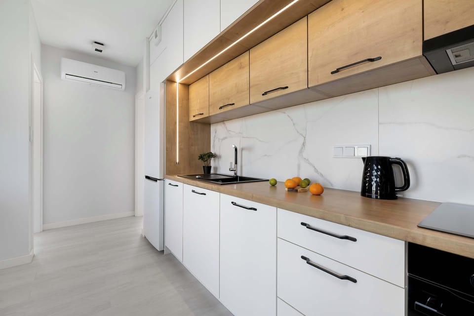 A sleek kitchen with white cabinets, wooden accents, and integrated appliances. Under-cabinet lighting highlights the clean countertops and minimalist layout.