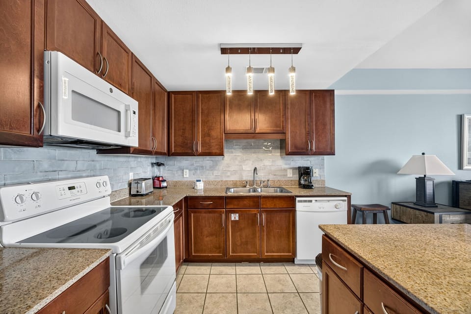 Cook up your favorite meals in this well-equipped kitchen featuring granite countertops, stylish tile backsplash, and modern lighting that sets the perfect mood for your vacation.