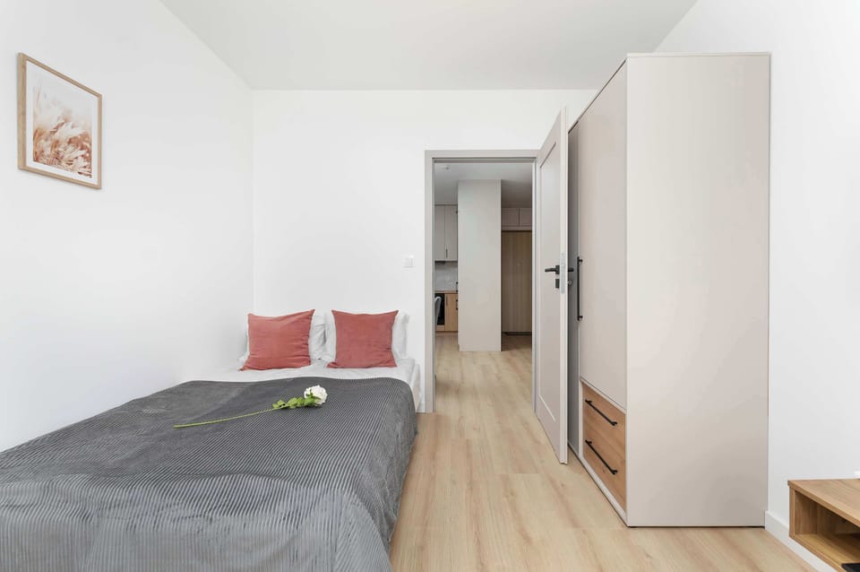 A simple bedroom with a sofa bed dressed in neutral bedding and pink accent pillows. The room is bright, clean, and focused on comfort.