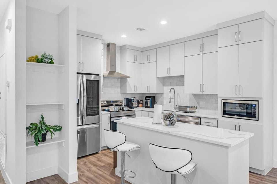 Fully equipped modern kitchen with sleek white cabinets, stainless steel appliances, and a spacious island—perfect for home-cooked meals during your stay.