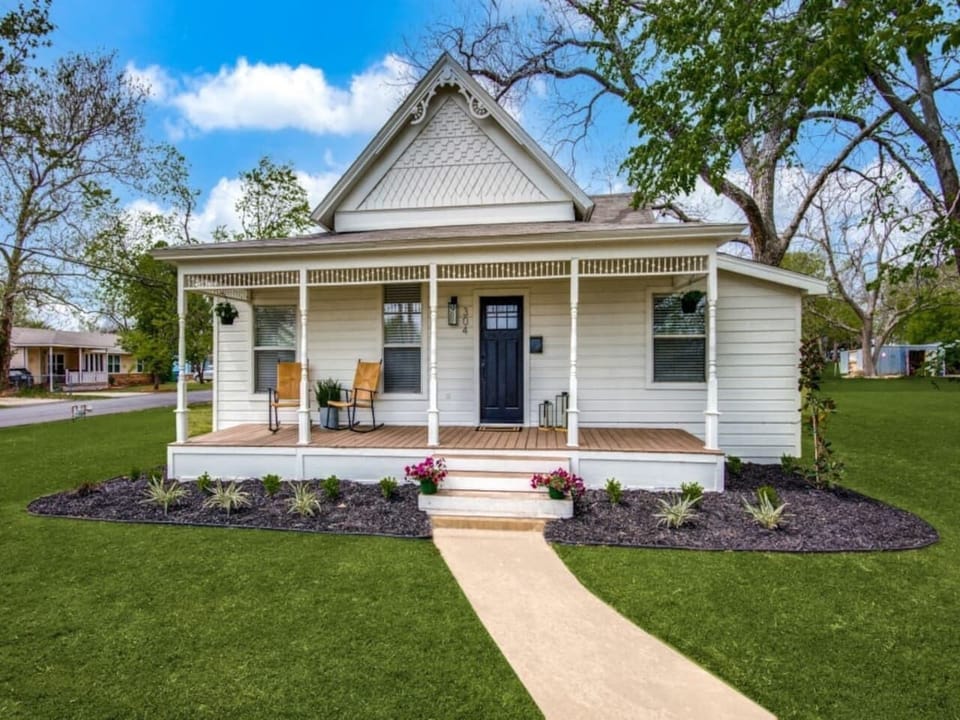Charming single-story modern farmhouse. White board-and-batten siding, covered front porch, flower-lined walkway, and manicured landscaping. Walkable to downtown Aubrey dining and coffee in Denton County.