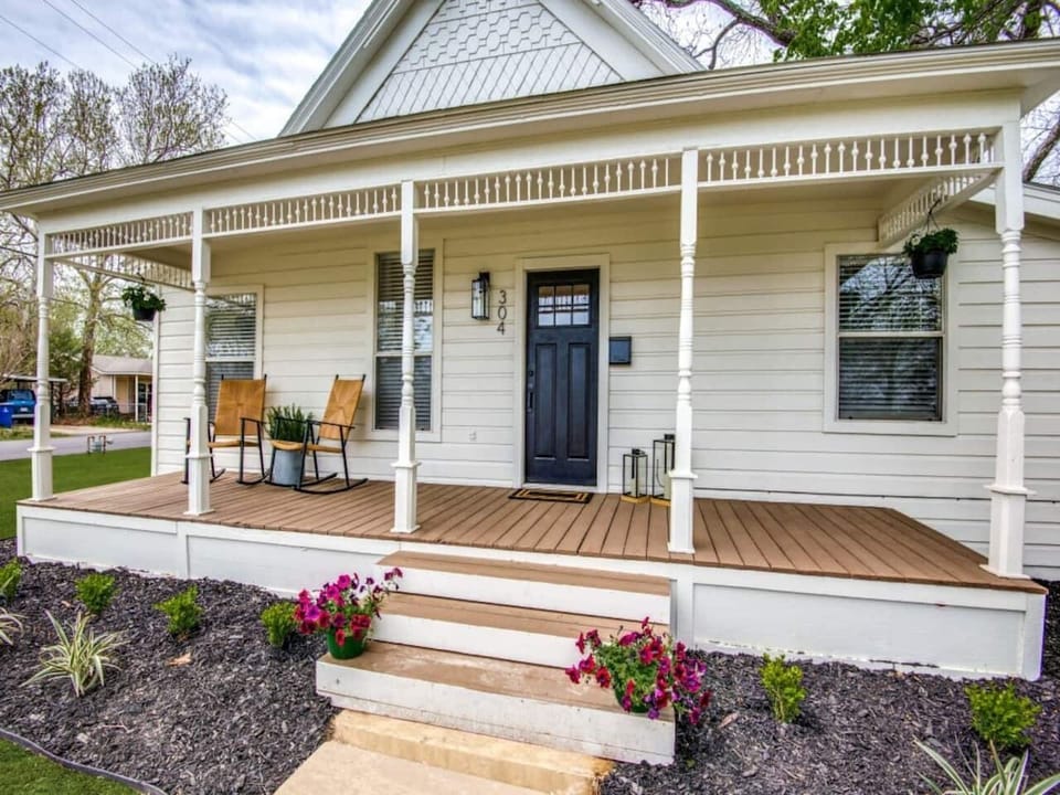 Welcoming covered front porch with seating, navy front door, flower boxes, and classic farmhouse trim. Modern farmhouse rental in downtown Aubrey TX near Frisco, Denton, and top Denton County wedding venues. Sleeps up to 7 guests.