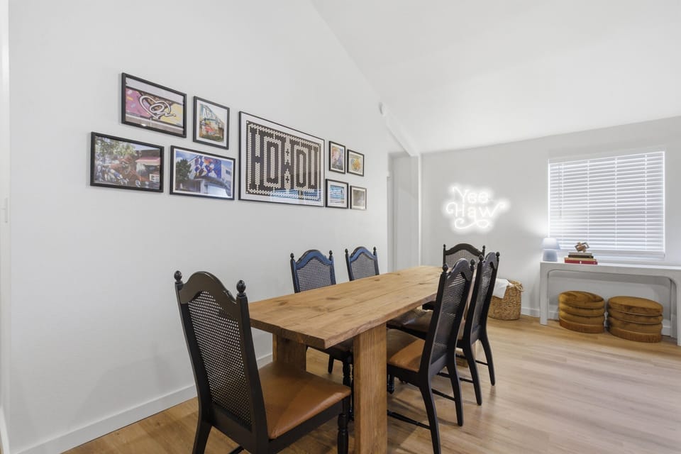 Dining area alternate angle with gallery wall art and natural light. Seats full group of 8. Open-concept flow to kitchen and living room.