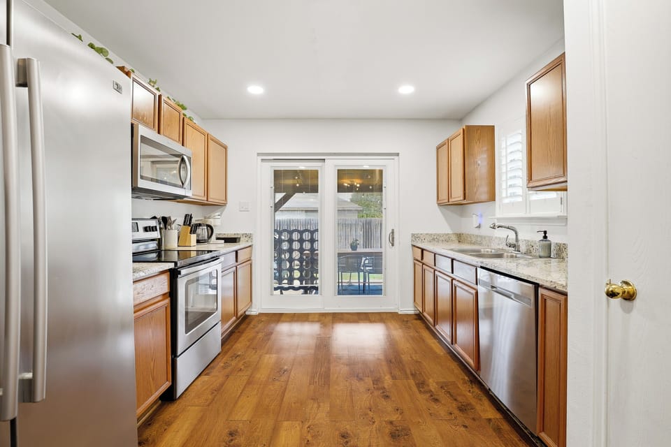Stainless kitchen with electric stove, full-size refrigerator, microwave, and granite countertops — open to the dining and living area for easy entertaining. Fully stocked with cooking basics and utensils.