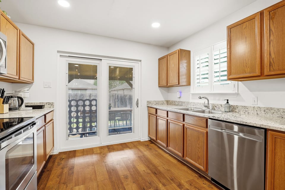 Full galley kitchen with electric stove, stainless dishwasher, granite countertops, ample cabinet space, and sliding glass door to the backyard. Everything stocked for home-cooked meals.