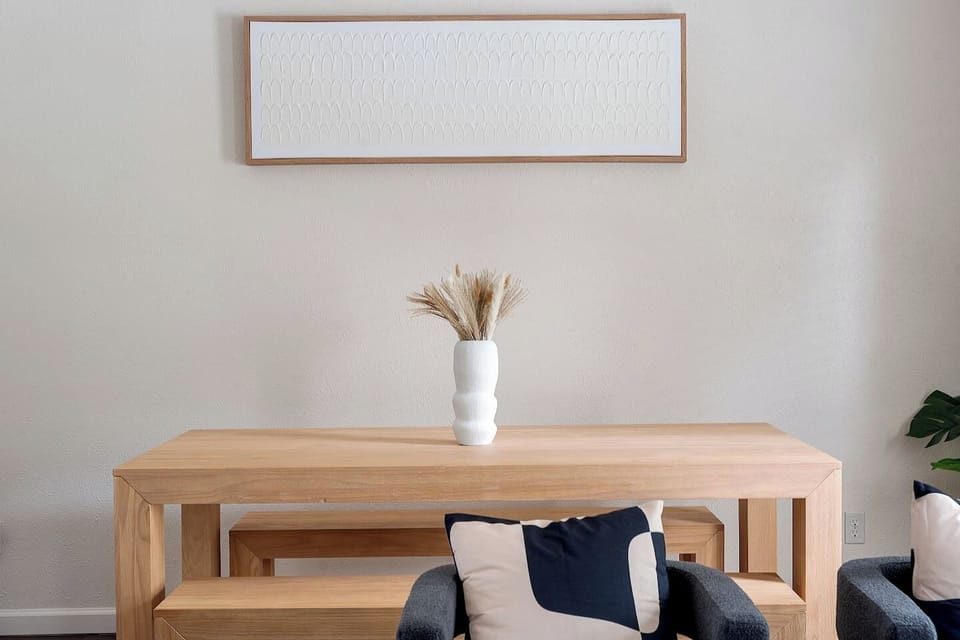 This elegantly designed room features a modern wooden table with a minimalist vase, stylish seating, and contemporary wall art.