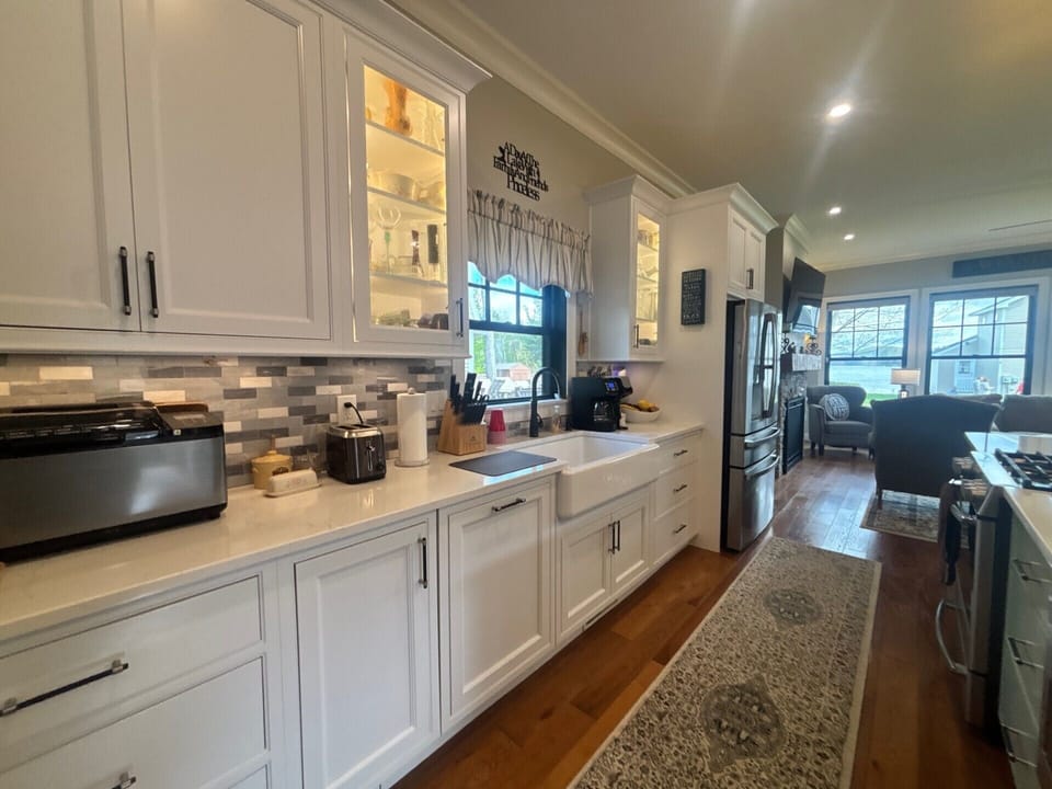 Your fully-equipped kitchen features white cabinetry, modern appliances, and warm wood floors—perfect for preparing homemade meals or morning coffee while enjoying natural light streaming through the windows.