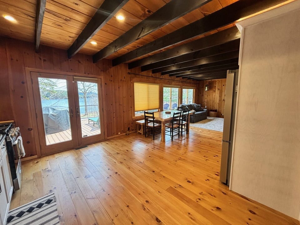 Step into your cozy retreat with warm wood floors and exposed beams overhead. Natural light fills the space, connecting your dining area and living room to peaceful lake views just beyond the deck.