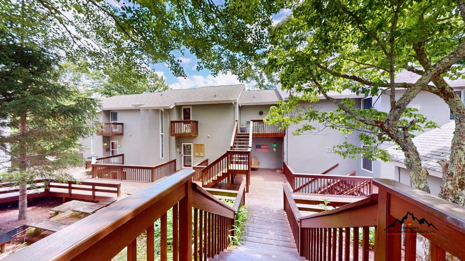 Tree-shaded property with elevated wooden walkways connecting multi-level buildings, featuring private balconies and peaceful mountain surroundings.