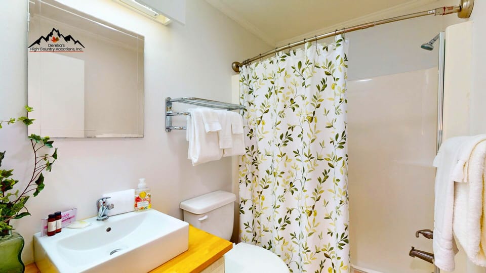 Step into your private bathroom featuring a fresh floral curtain, crisp white towels, and a welcoming space where you can unwind after exploring the mountains nearby.