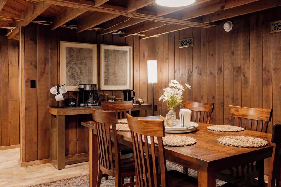 Warm wood-paneled dining space with a cozy, cabin-inspired feel. Features a large dining table, exposed beams, and a dedicated coffee station—perfect for gathering, sharing meals, and starting your mornings together.