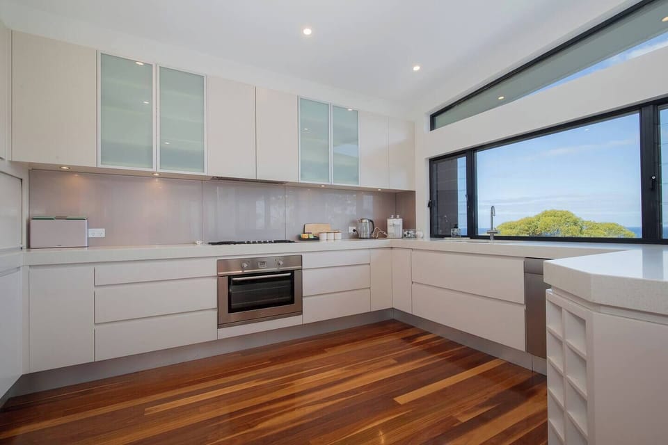 Cook with the coastline in sight from the sleek kitchen, where generous bench space and modern appliances make everything from morning coffee to family dinners feel effortless.