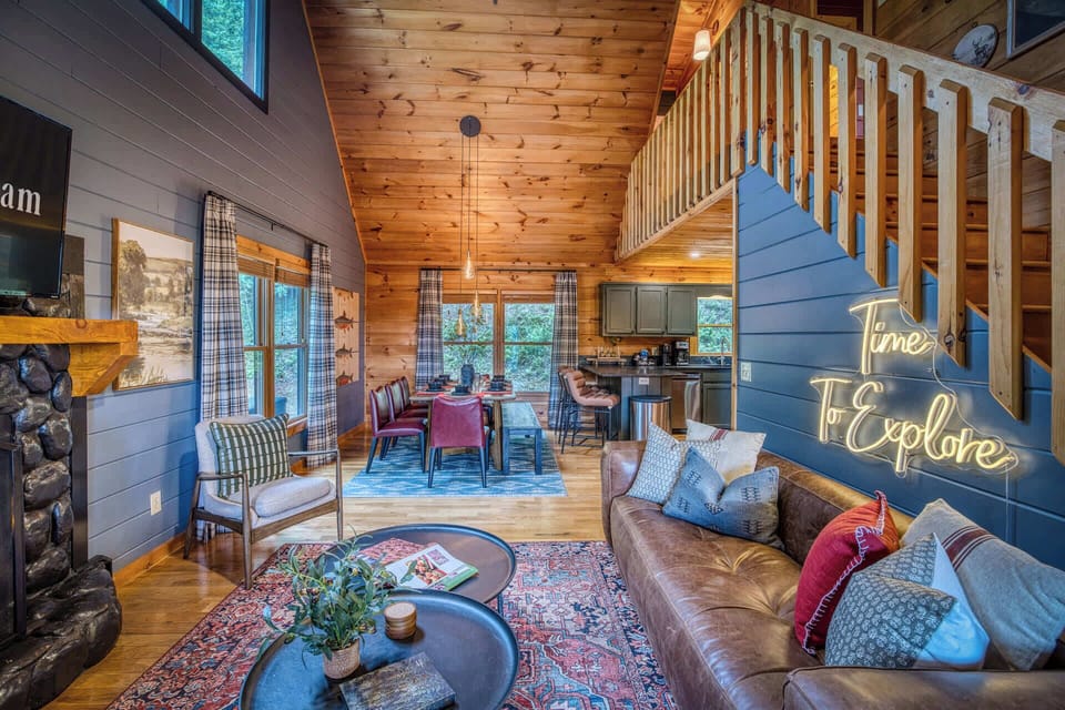 Step into a beautifully designed cabin retreat where rustic charm meets modern comfort. This open space is the perfect backdrop for your getaway, featuring soaring wood ceilings, a striking fireplace, and a cozy leather sofa made for relaxing.