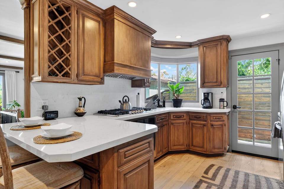 Gourmet kitchen featuring custom warm wood cabinetry, gleaming white countertops, and a glass-paneled door leading straight to the side yard.