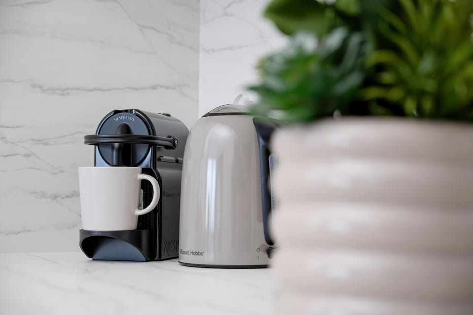 A modern coffee corner with a capsule machine and kettle adds comfort to the kitchen space. A green plant gives the interior a fresh touch.