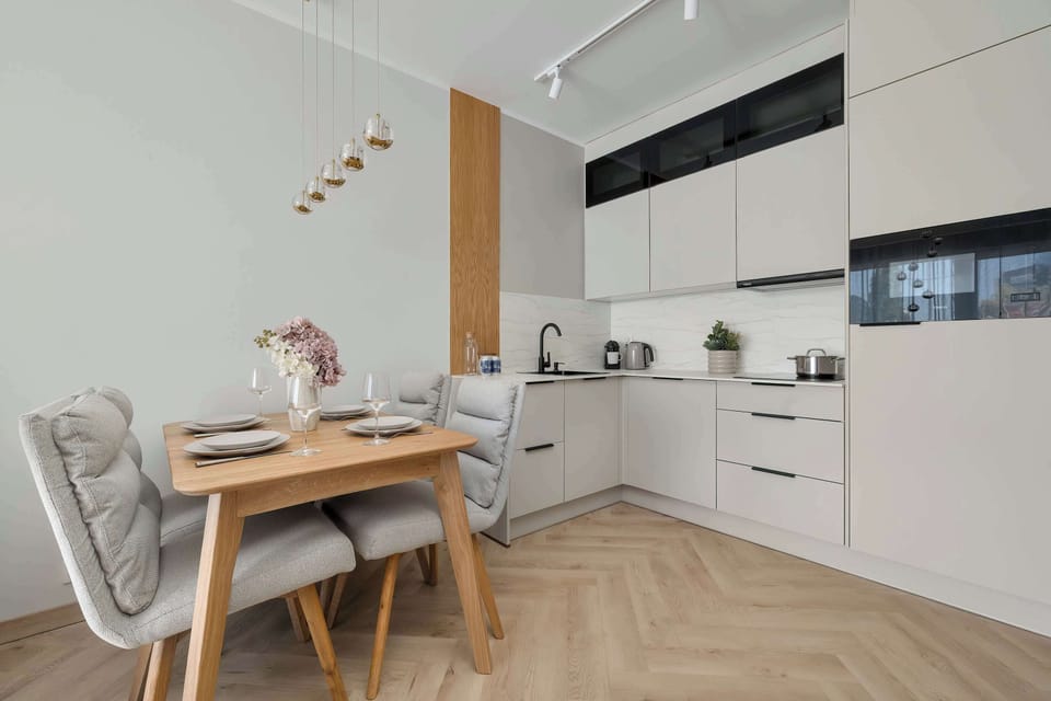 A modern kitchenette with white cabinets and wooden elements provides a clean and functional space for cooking. The dining area next to it adds comfort and practicality.