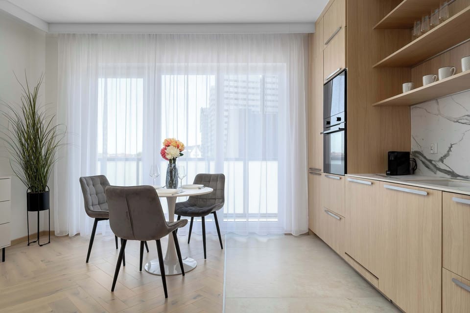 A modern kitchen combined with a dining area, featuring built-in cabinetry and a wooden dining table with chairs. The space is bright, functional, and designed for both cooking and shared meals.