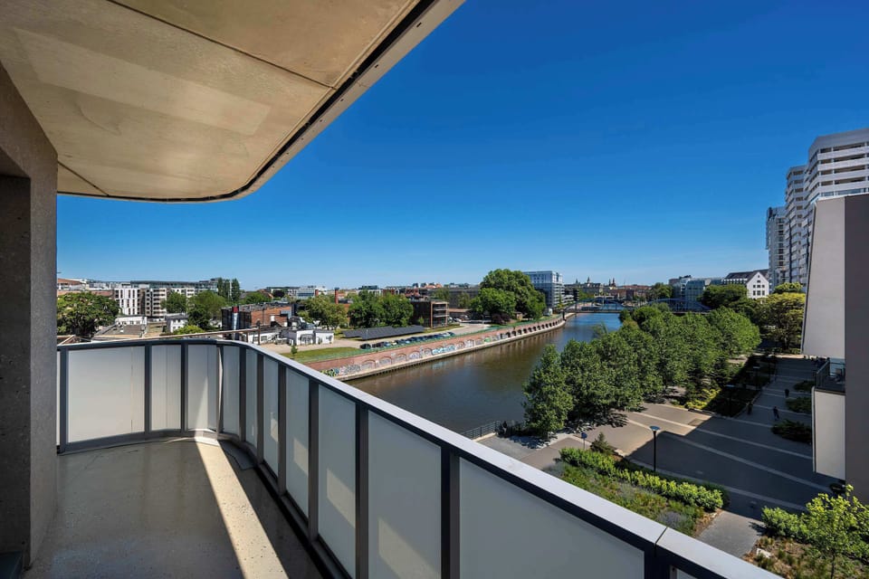 A wide balcony view showcasing nearby buildings and an open blue sky. The outdoor space feels spacious and ideal for enjoying the scenery.