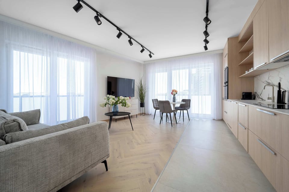 A spacious open-plan living room combining seating and dining areas in a bright, contemporary setting. The interior is minimalist with light colors and a strong sense of openness.