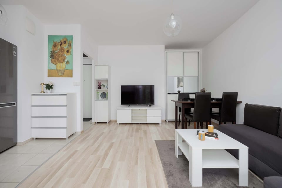 A stylish living room with a gray sectional sofa, white coffee table, and television positioned against the wall. Neutral tones and uncluttered décor create a modern atmosphere.