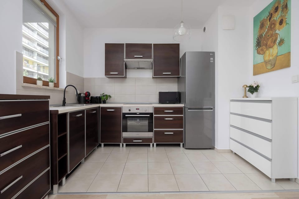 A compact kitchen with dark cabinetry, stainless steel appliances, and light tiled flooring. Wooden finishes and modern fixtures add elegance to the practical layout.